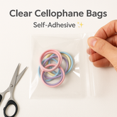 📦 Clear Cellophane Bags – Self-Adhesive | Multiple Sizes with colorful rings inside the bag and scissors beside it.